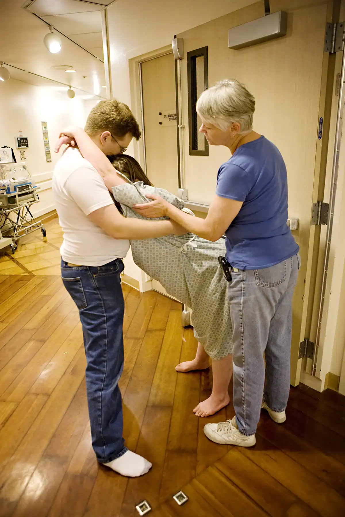 Doula massaging her client's back with a massage tool while client's partner helps her relax against him during a contraction.