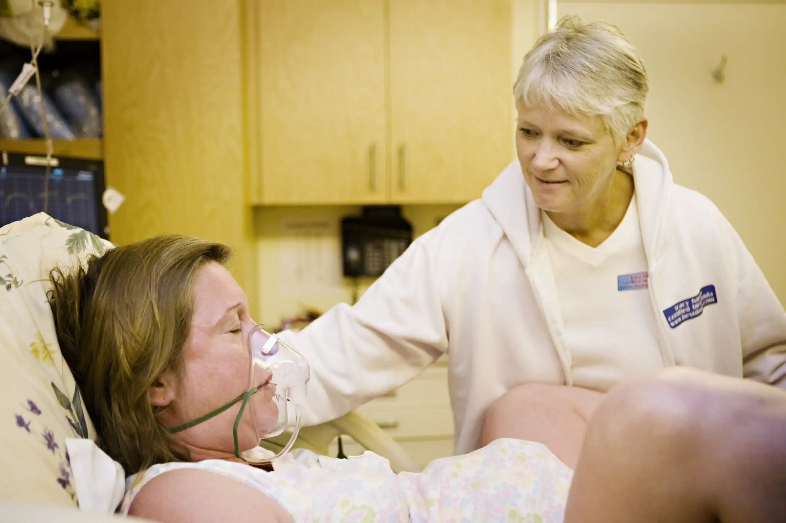 A laboring woman wearing an oxygen mask while pushing with support of a doula.