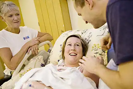 A happy moment for expectant parents with new baby in mother's arms while doulas observes.