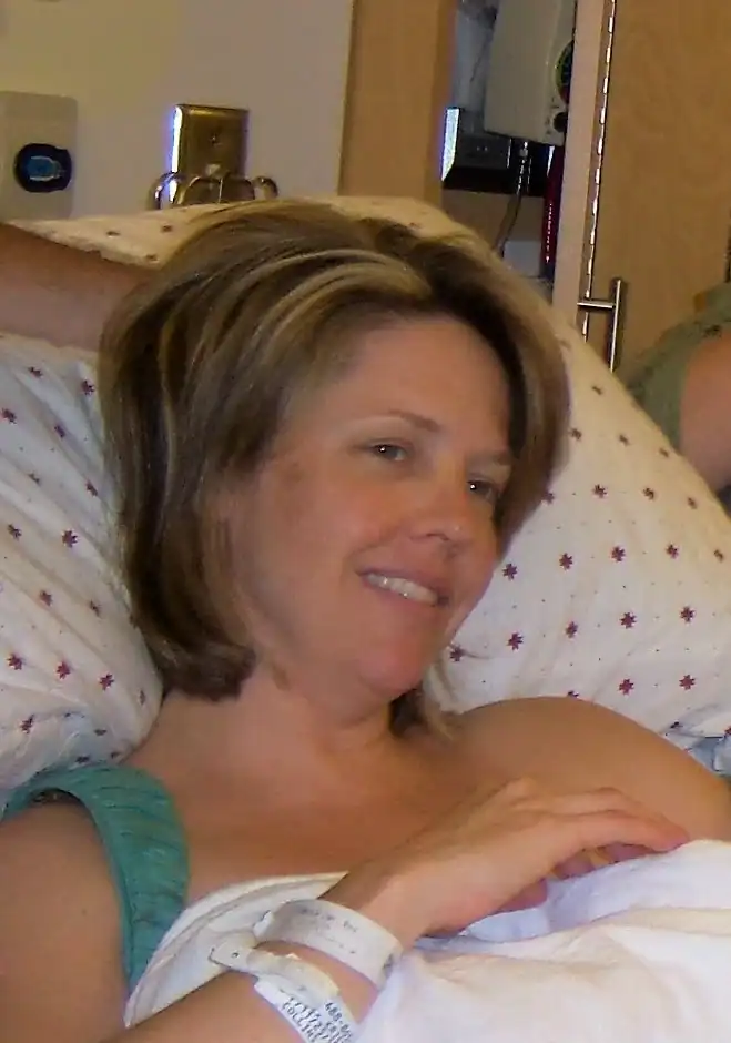 Supportive doula assisting new mother during postpartum recovery.