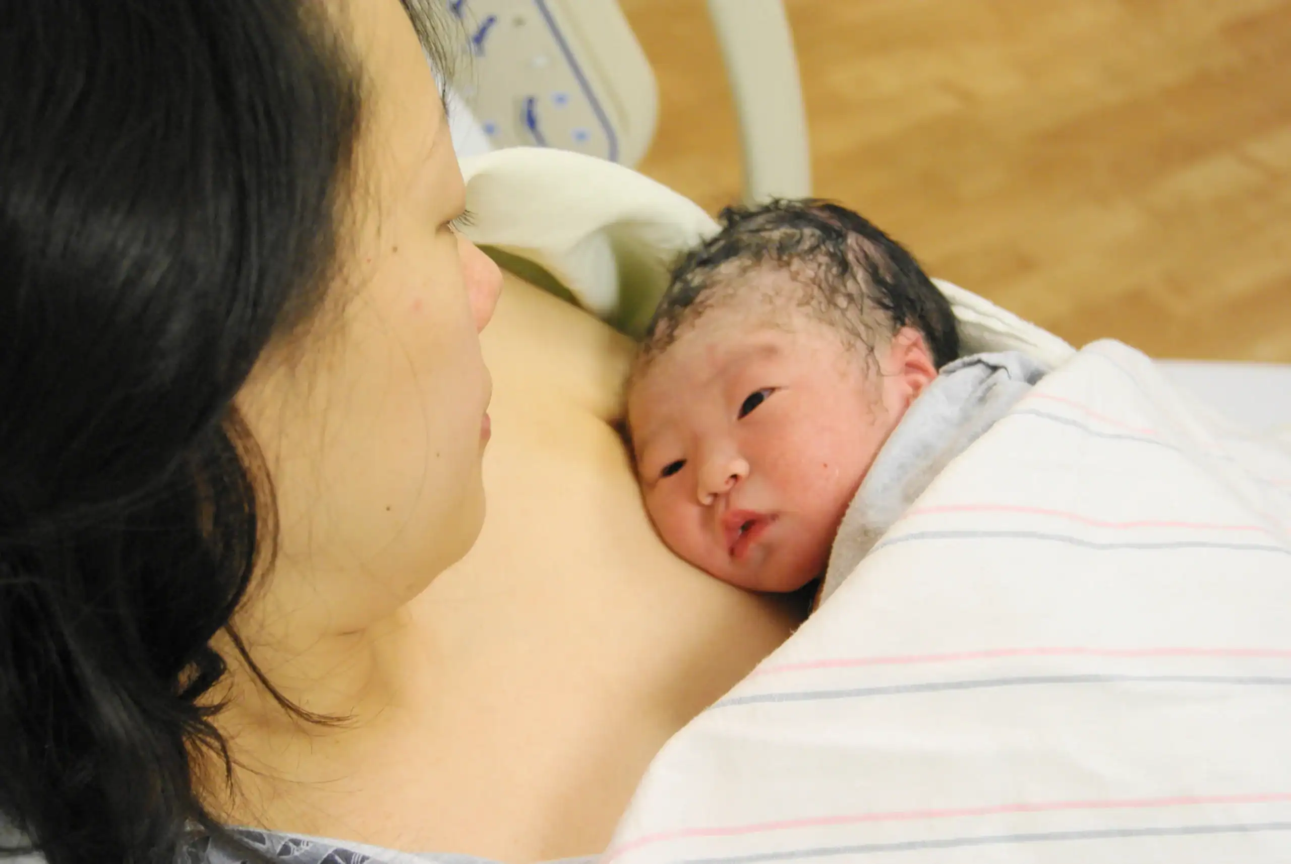 Newborn baby on mother's chest, looking into her eyes.