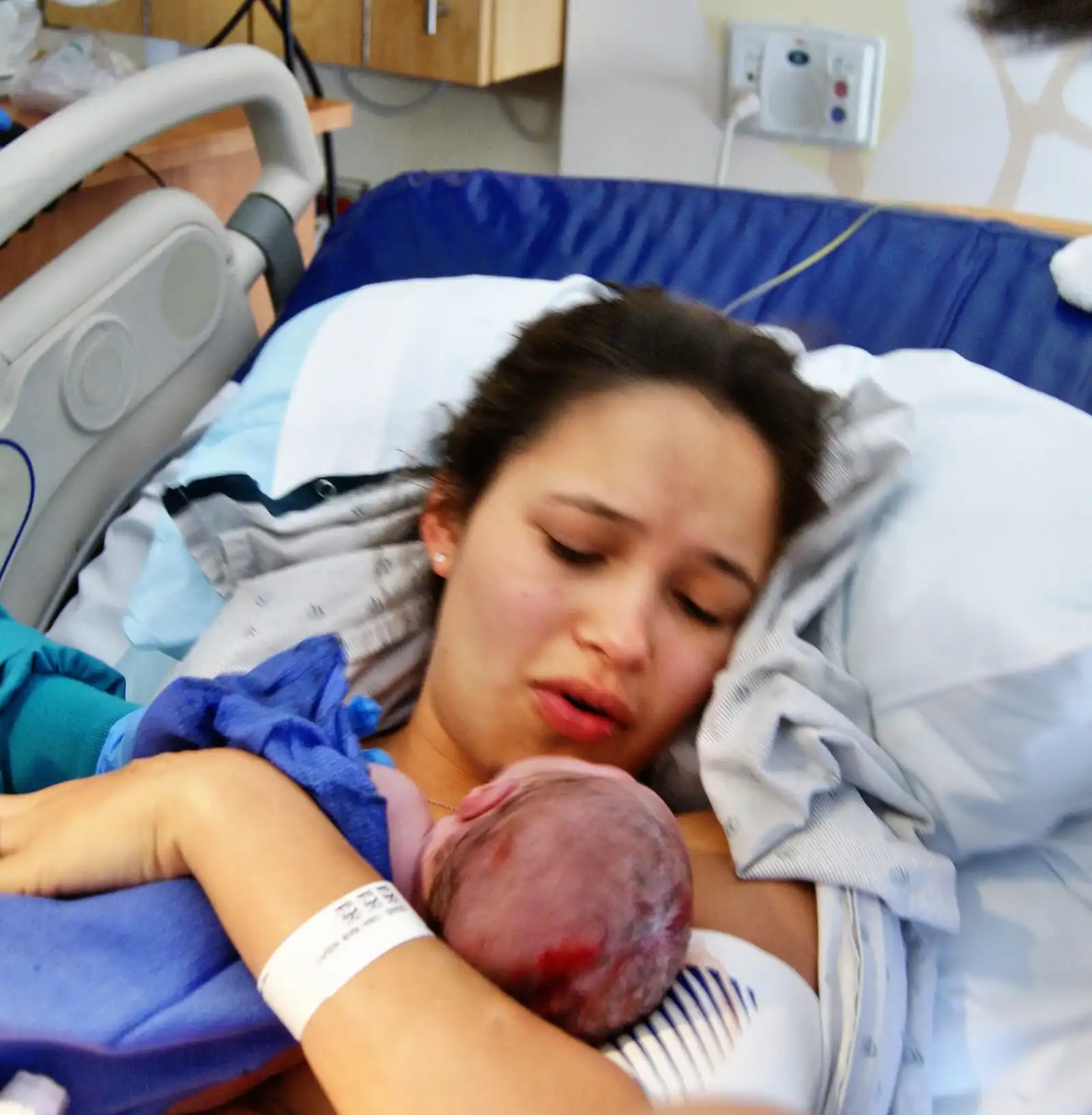 Mother holding newborn baby after delivery in hospital.