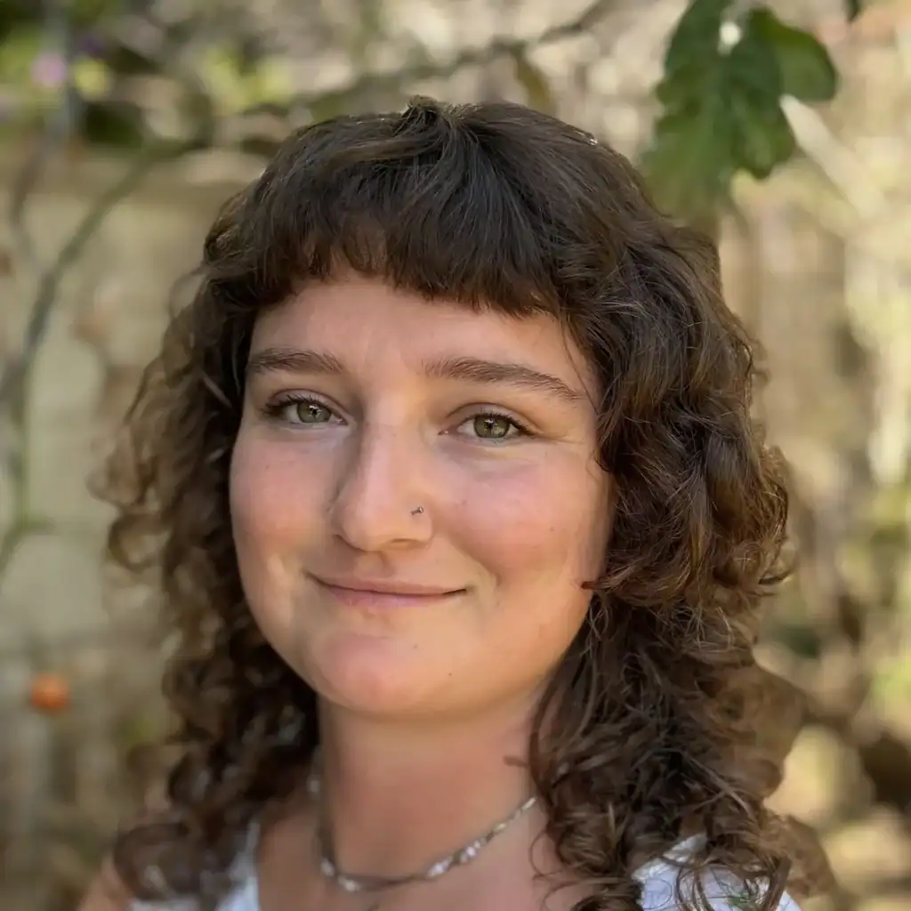 Close-up of Isabel, a young woman with curly hair, smiling outdoors, representing compassionate doul.