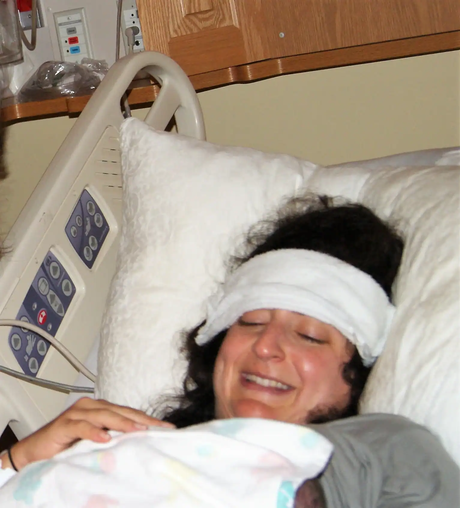 Postpartum woman resting with head bandage in hospital bed.