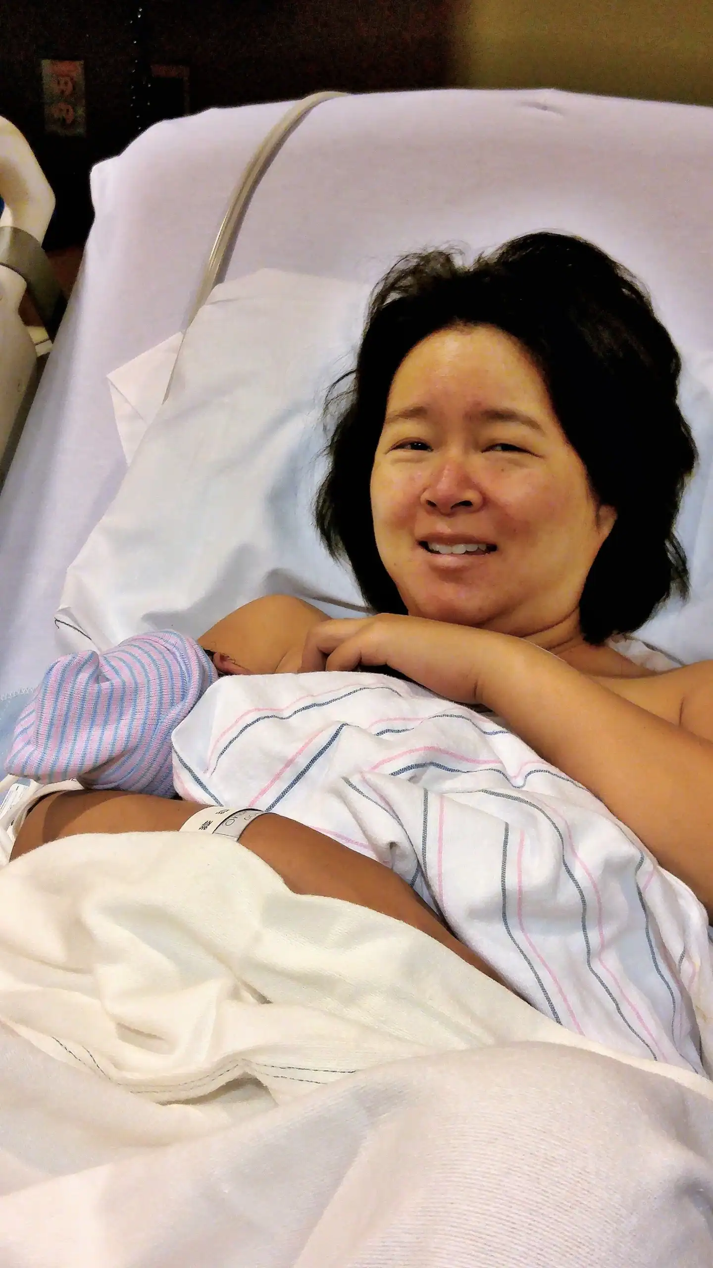 Woman resting in hospital bed after childbirth, supported by doula.