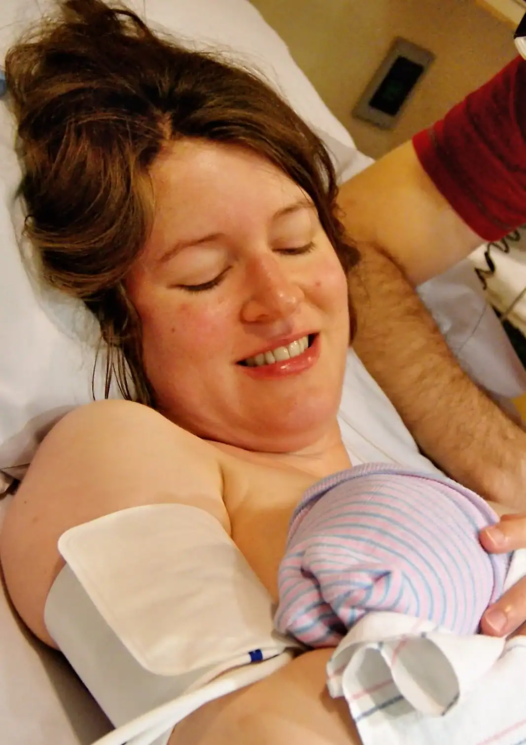 Mother holding her newborn baby in hospital bed, showcasing postpartum care and support.