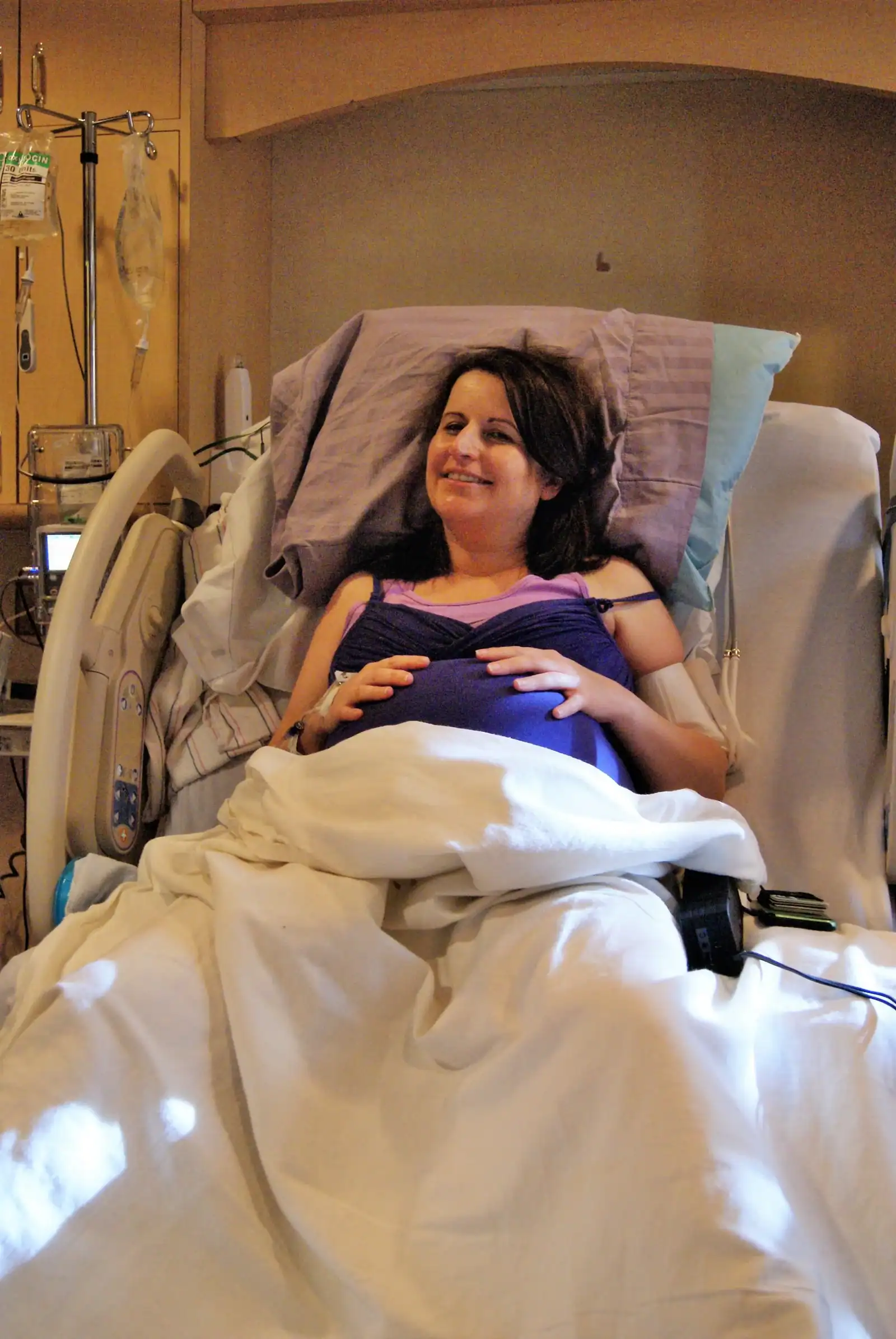 Woman in hospital bed smiling, receiving professional doula support during childbirth.