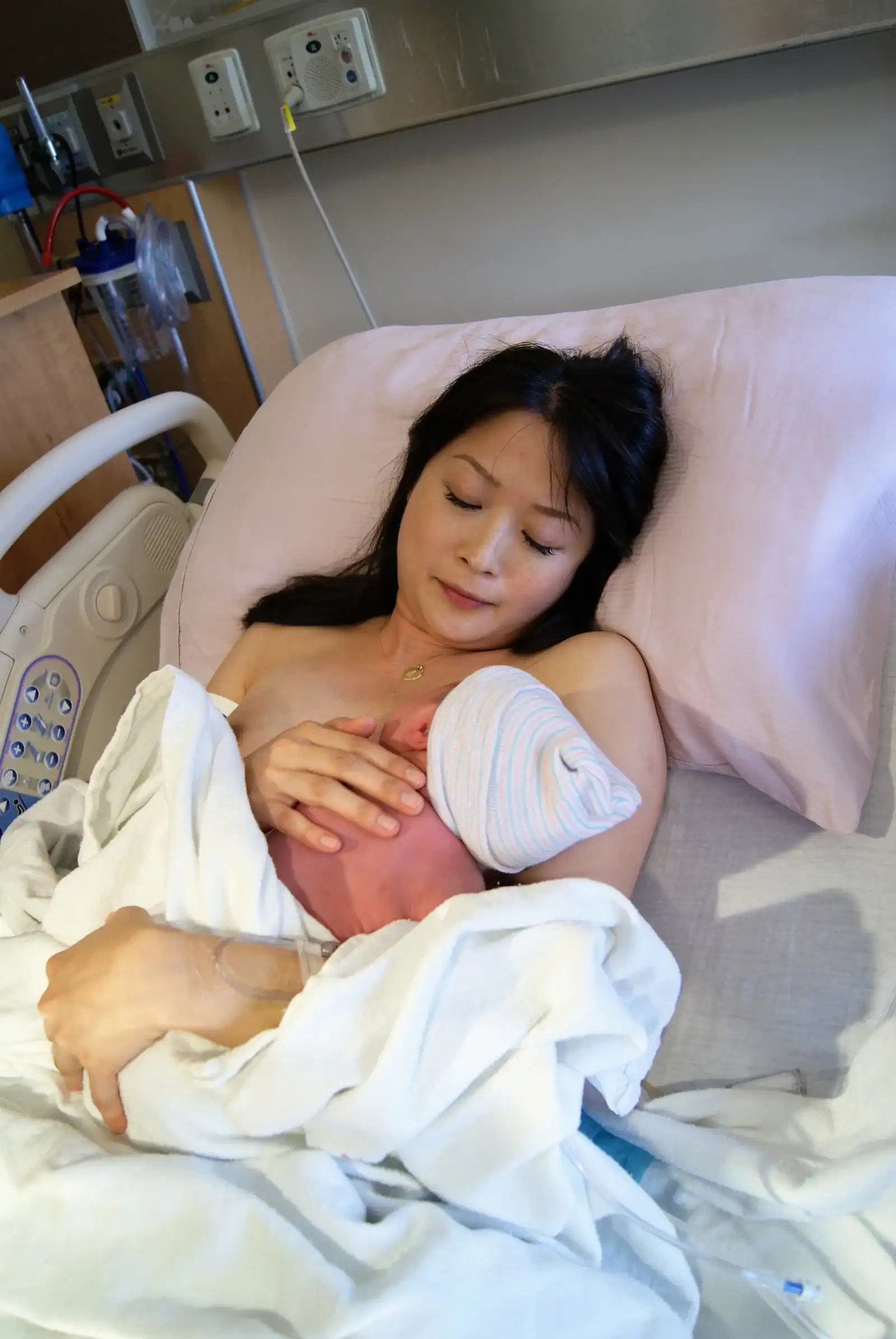 Supportive mother with newborn in hospital bed.