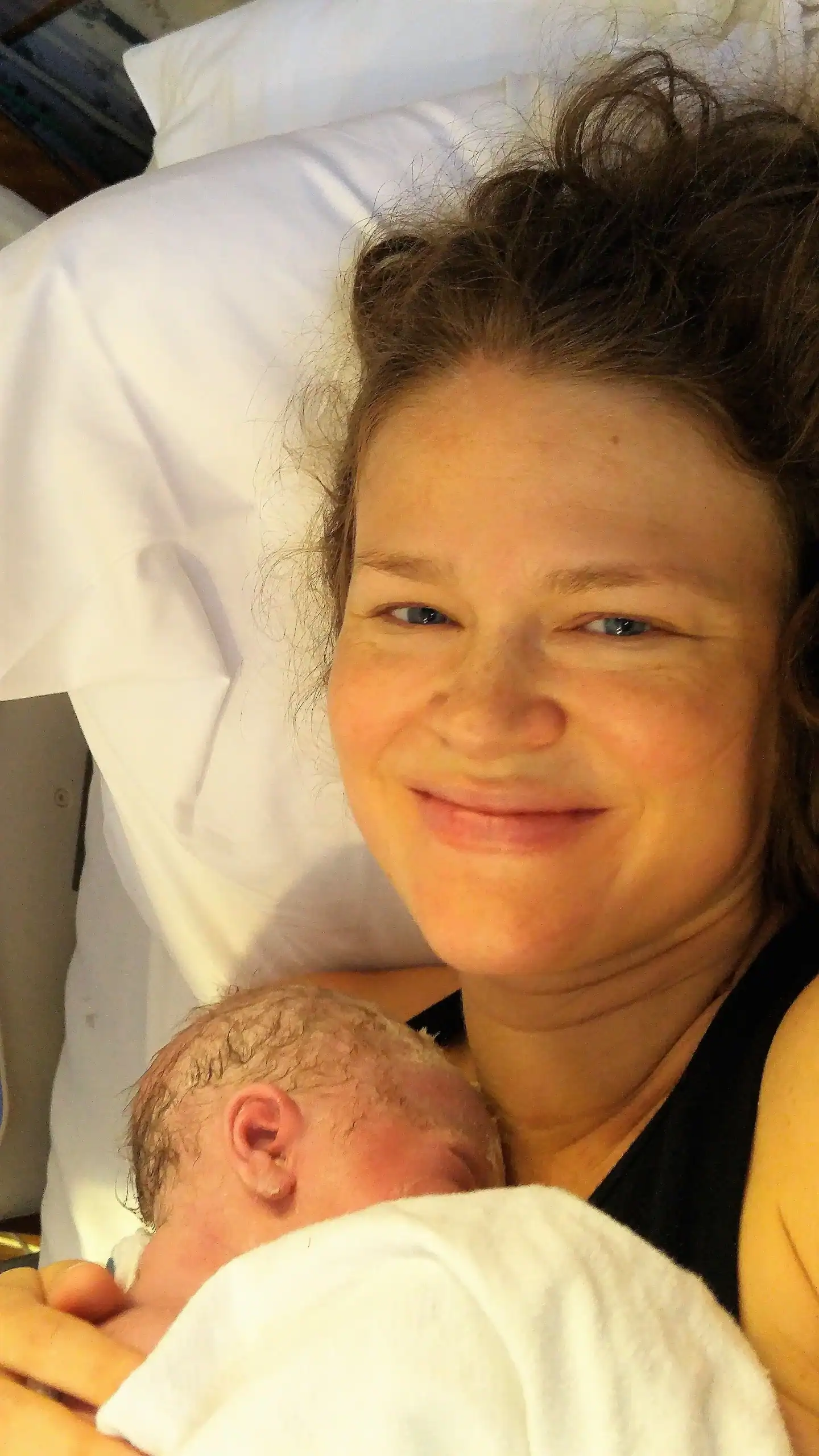 Mother with newborn baby in hospital bed, smiling and holding her child after childbirth.