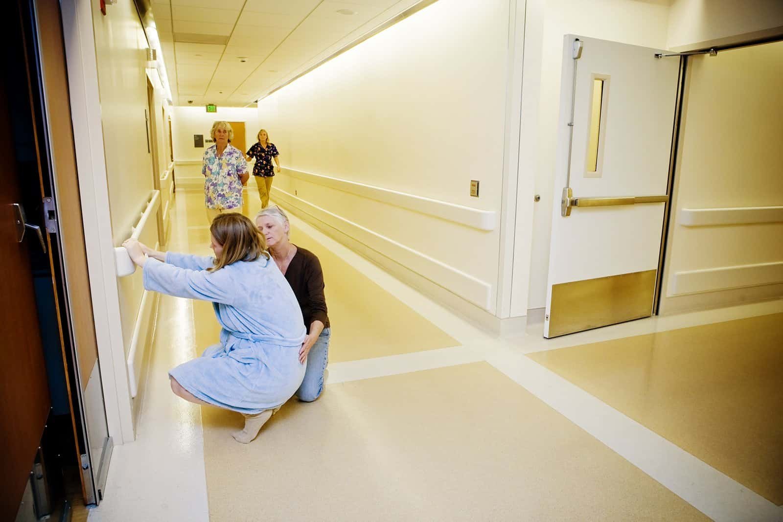 Doula providing emotional support to a pregnant woman in hospital hallway.